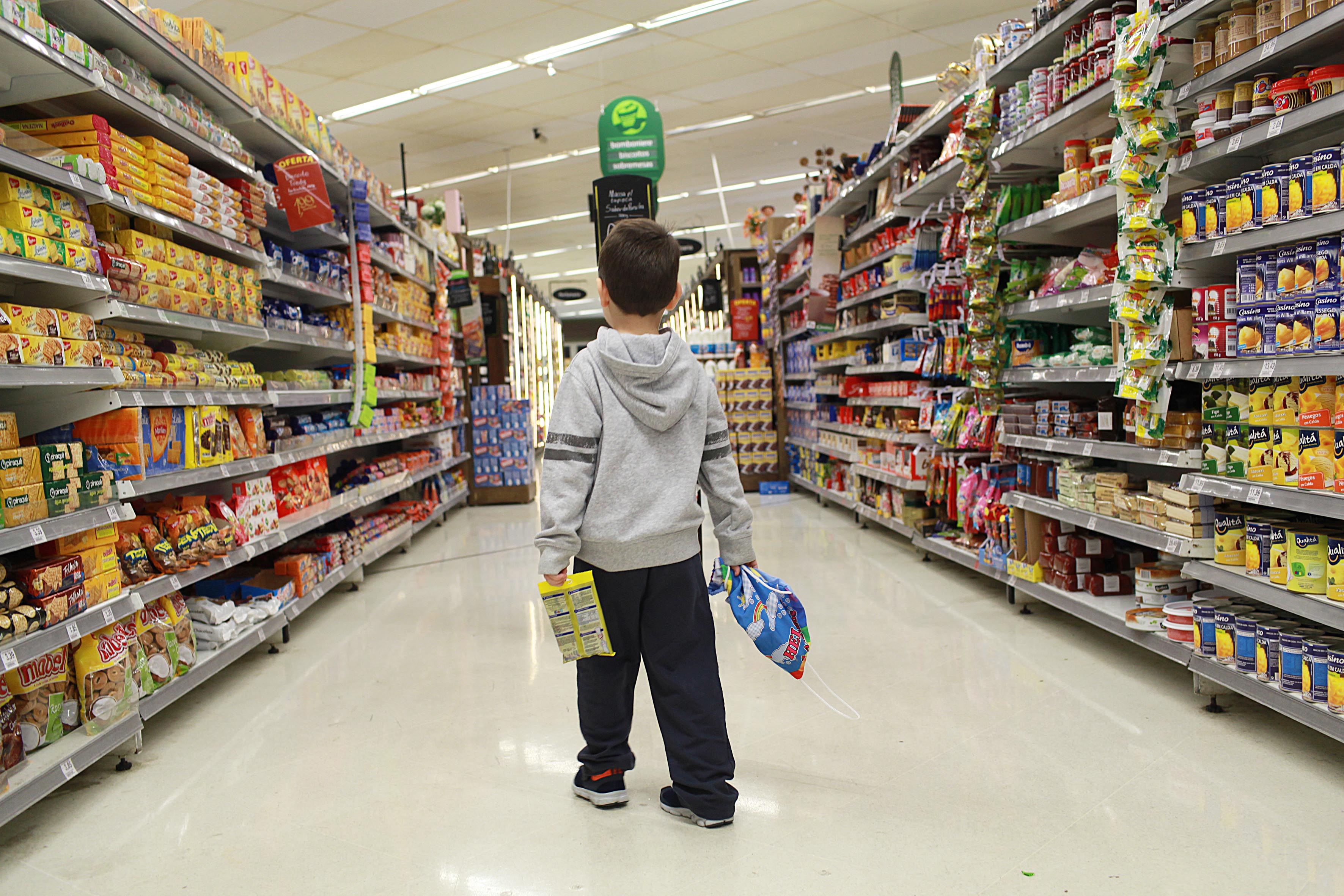 Criança em corredor de mercado com várias propagandas (Foto: Mães de Peito)
